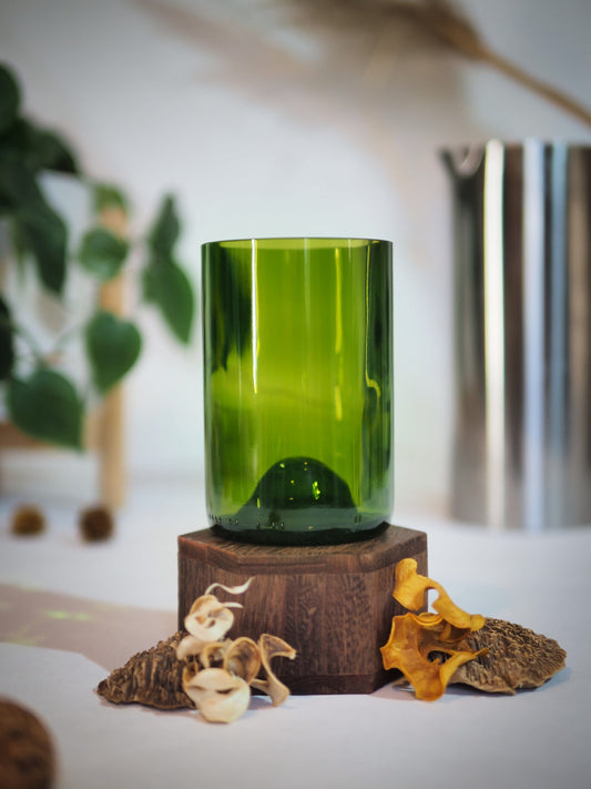 Verre vert recyclé artisanal, découpé dans une bouteille en verre, posé sur un socle en bois naturel. Mise en scène décorative avec champignons séchés et fond flou végétal. Produit écologique et design, idéal pour une décoration durable ou un cadeau écoresponsable.